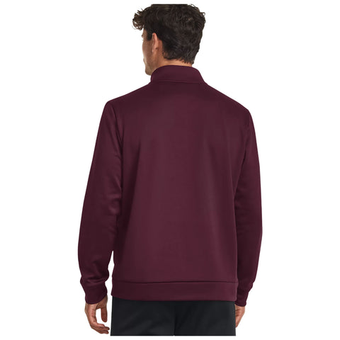 A man stands with his back facing the viewer wearing a dark burgundy pullover with a collar in a plain background emphasizing the clothing.