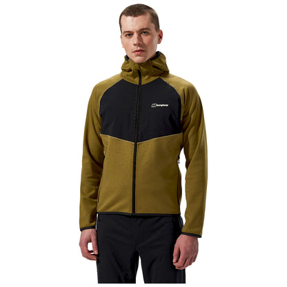 A man is standing confidently wearing a two-tone zip-up jacket with a hood colored in olive green and black while looking directly at the viewer in a neutral background.