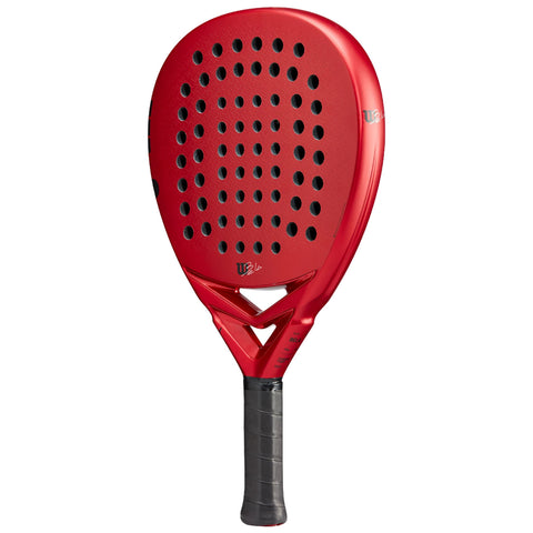 A red paddle with a perforated surface is positioned upright. It is designed for sport, featuring a textured grip for handling. The bright color indicates athletic equipment.