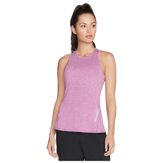 A woman is wearing a sleeveless pink athletic top while posing with a neutral expression in a simple background highlighting her attire. The shirt has the logo SKECHERS on the side.