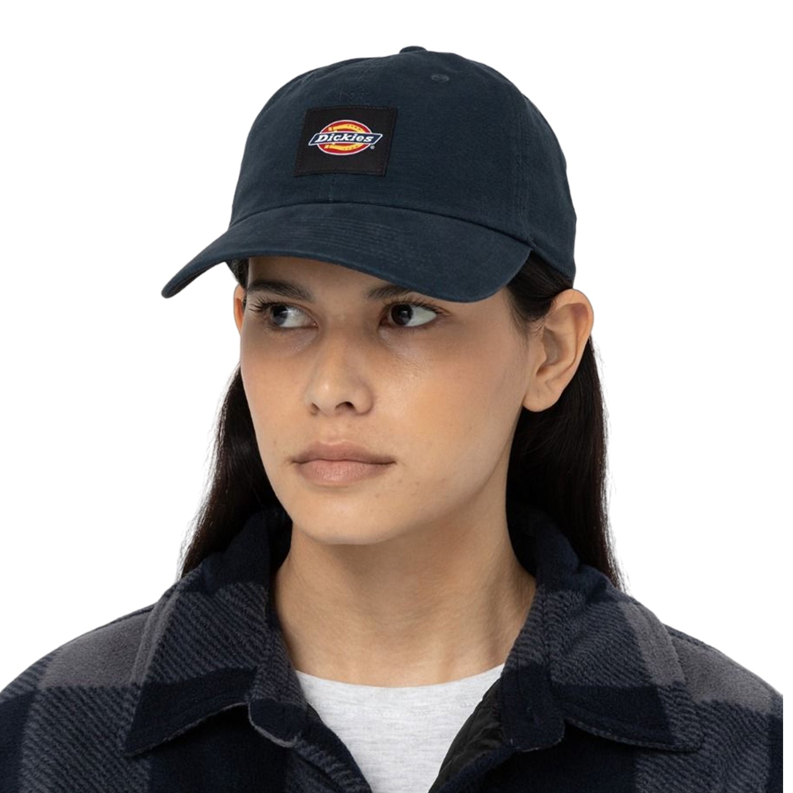 A woman is wearing a dark baseball cap featuring a logo and a checkered shirt. She is looking forward with a neutral expression against a light background.