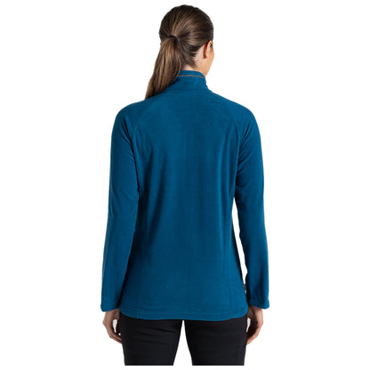 A woman is standing with her back facing the viewer wearing a blue fleece jacket with long sleeves in a plain background, her hair is tied back and she appears to be relaxed.