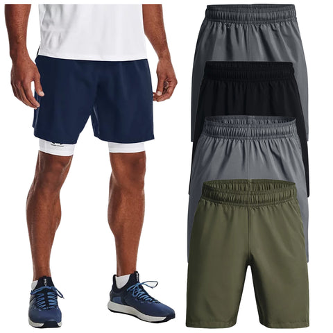 A person stands wearing navy athletic shorts over white compression shorts with blue athletic shoes while four other pairs of shorts in gray black and olive green are displayed nearby.