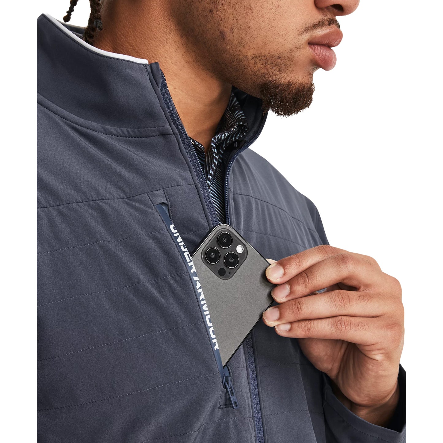 A hand is inserting a smartphone into a zippered pocket on a navy jacket while a person stands in a neutral setting highlighting a casual, practical action of storing a device.
