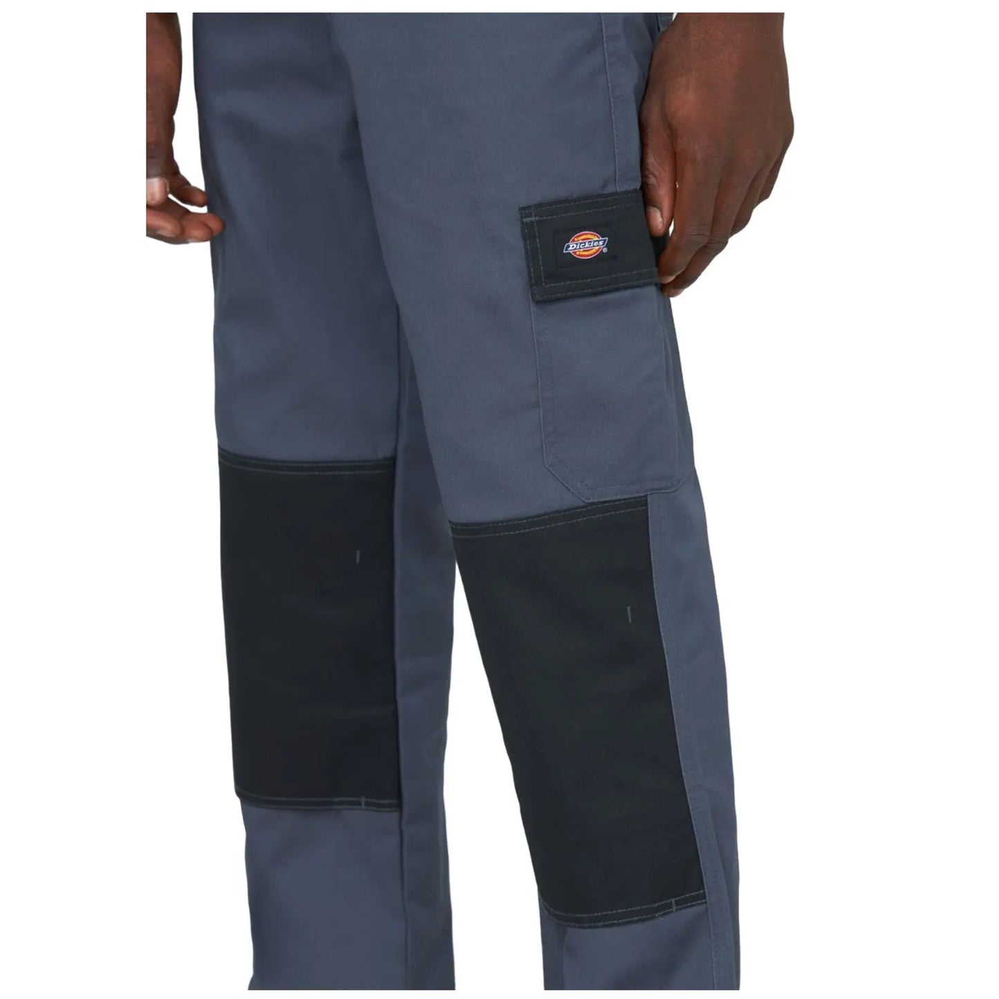 Gray work pants with black reinforced patches on the knees are being held by a hand. The pants feature a small logo on the side pocket.