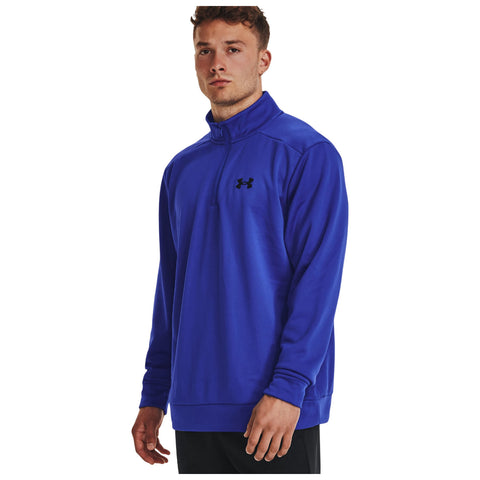 A male figure stands confidently wearing a bright blue long-sleeve athletic pullover with a high collar and a half-zip design showcasing a logo on the left chest against a white background.