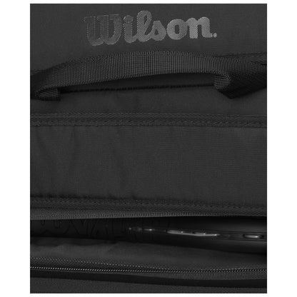 A black bag with a visible Wilson logo lies open displaying its interior contents including a tennis racket featuring a black handle and strings in a dark environment.