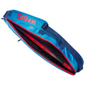A blue Wilson bag with a red zipper is open revealing a red tennis racket inside resting on a black inner lining against a neutral background.