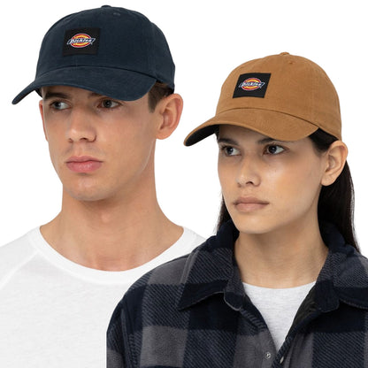 A man and a woman are wearing baseball caps facing forward. The man wears a navy cap and a white shirt while the woman wears a tan cap and a black plaid shirt.