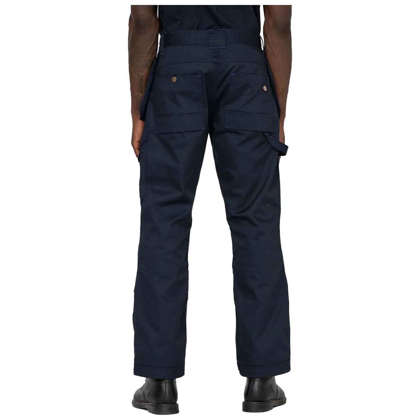 Dark blue work pants are worn by a person facing away showing multiple pockets and loops in an indoor setting with a plain white background. The person is standing still.