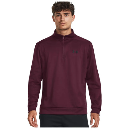 A young man is wearing a maroon quarter-zip pullover with a high collar standing against a plain white background showcasing the garment and its brand logo on the chest.