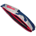 A tennis bag is open revealing a red interior and compartments holding tennis rackets and accessories with a blue strap and a prominent Wilson logo on the exterior.