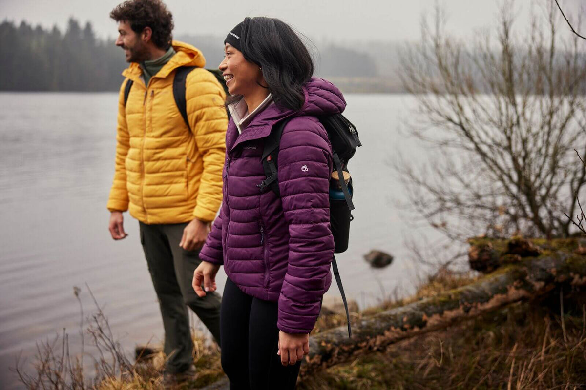 Two people in colorful jackets standing by a lake with backpacks.