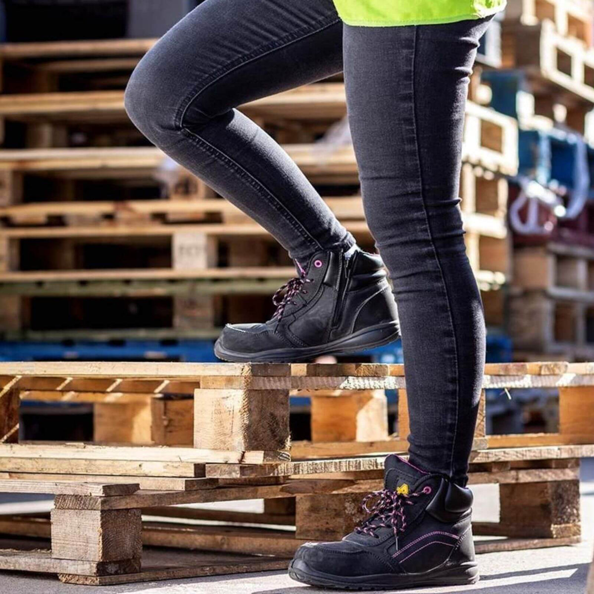 Person wearing black boots and dark jeans standing on wooden pallets in a warehouse setting.