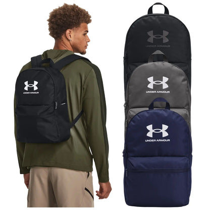 A young man is wearing a black Under Armour backpack while facing slightly away from the viewer. Three additional backpacks in black, grey, and navy are displayed beside him.