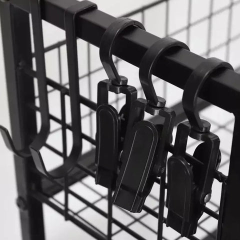Black metal clips hang from a horizontal bar attached to a grid-like structure providing functional storage in a minimalistic environment with a neutral background.