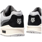 Black and gray athletic shoes are displayed from an angled rear view with a prominent logo on each heel showcasing a stylized shield and brand name K-Swiss on the side.