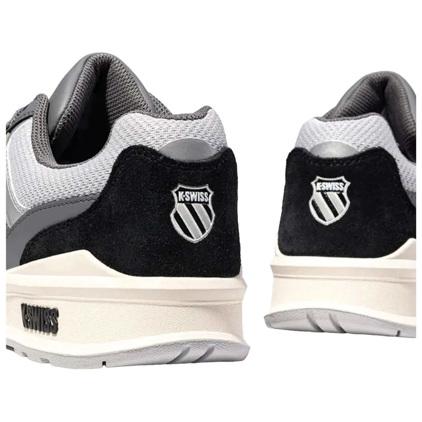 Black and gray athletic shoes are displayed from an angled rear view with a prominent logo on each heel showcasing a stylized shield and brand name K-Swiss on the side.