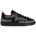 A sneaker features a mix of black and gray suede with dark laces and brown accents on the collar while resting on a textured black rubber sole.
