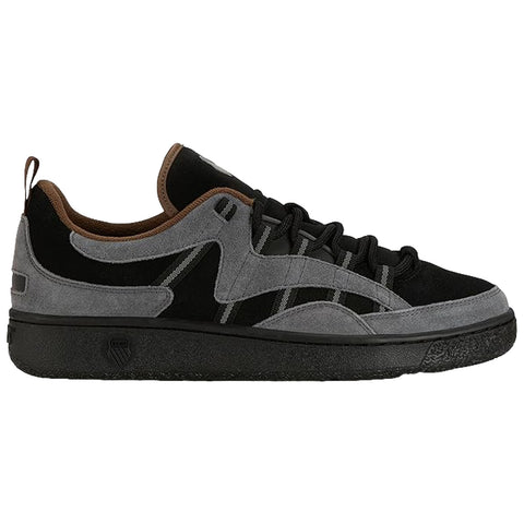 A sneaker features a mix of black and gray suede with dark laces and brown accents on the collar while resting on a textured black rubber sole.