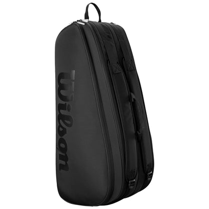 A large black sports bag is standing upright featuring dual handles and a zipper close while prominently displaying the brand name Wilson on its side in bold lettering.