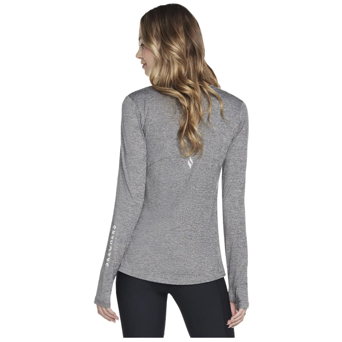 A woman with long hair is wearing a fitted gray long-sleeve shirt and black leggings while standing with her back turned, showcasing the shirt's design.