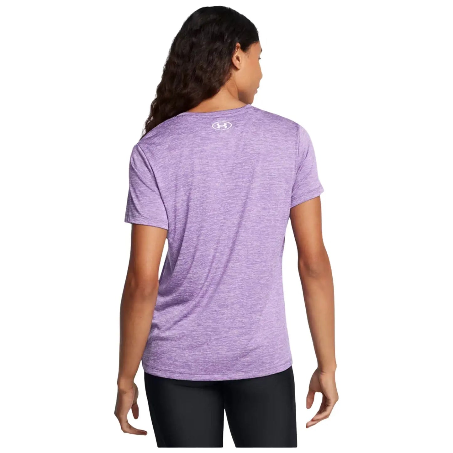 A person stands with their back facing the viewer wearing a purple athletic shirt and black leggings in a neutral background. Their hair is long and slightly wavy.