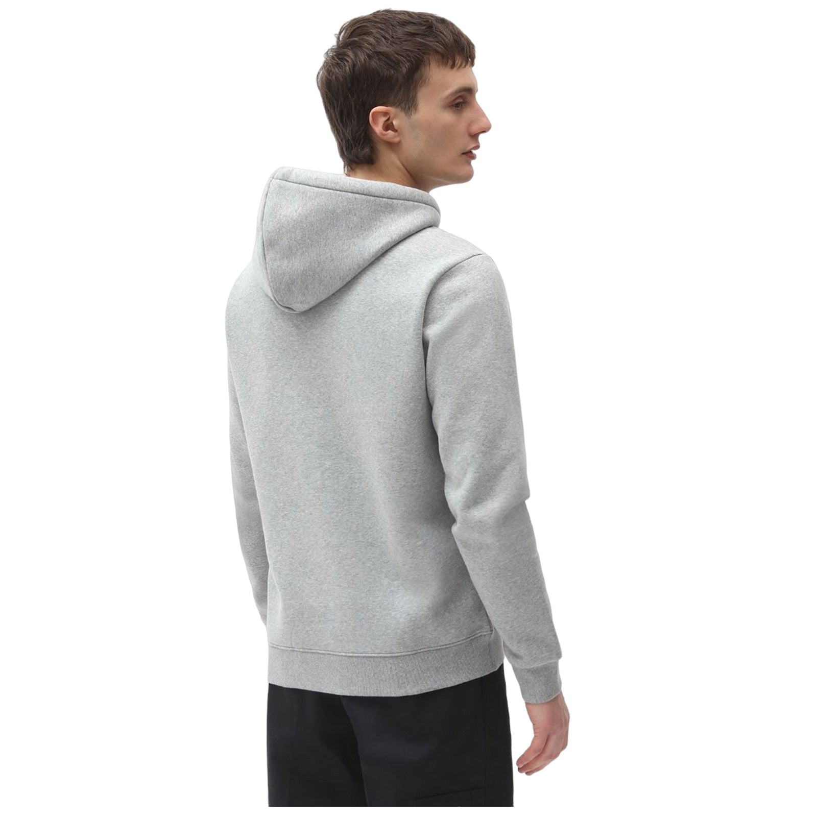 A young man is standing with his back turned wearing a light gray hoodie and dark pants in an undefined setting which emphasizes a casual and relaxed appearance.