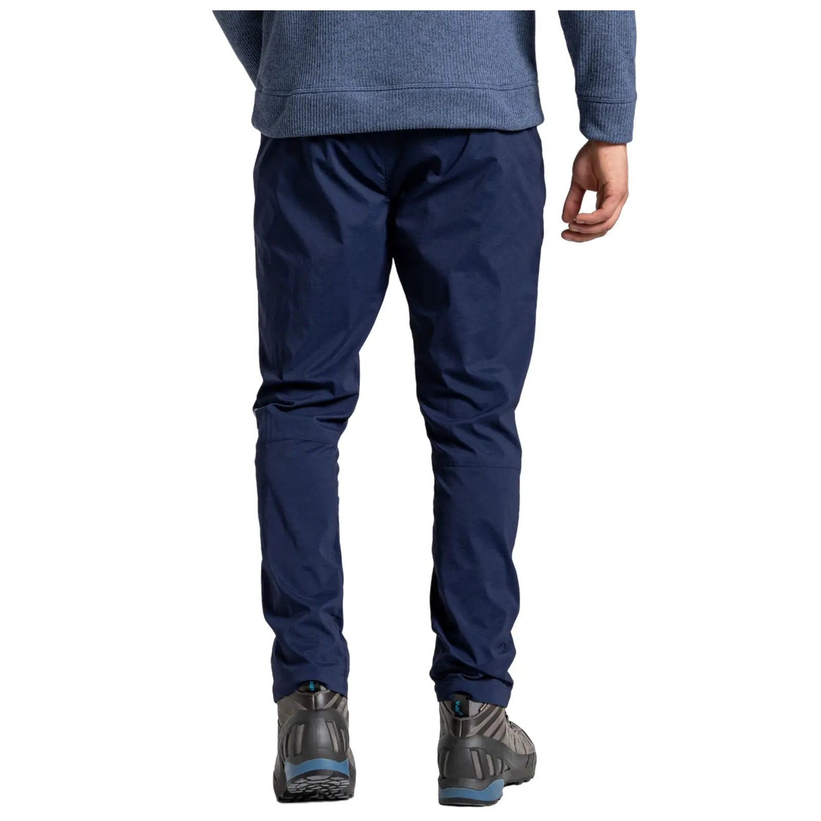 Navy pants are being worn by a person standing with their back facing the viewer in a casual indoor setting, paired with gray and blue outdoor shoes.