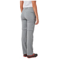 A person is standing with their back facing the viewer wearing gray outdoor pants and black footwear in a neutral backdrop. The pants have cargo pockets and a zippered section.