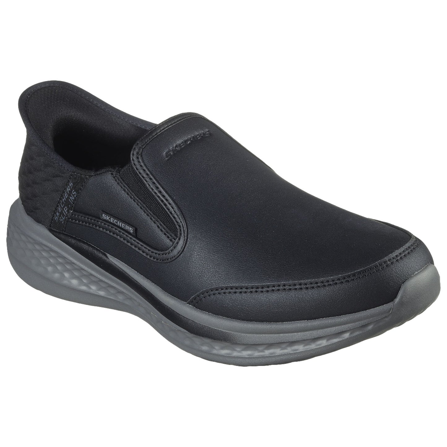 A black slip-on shoe features a smooth leather upper and elastic side panels for easy wear resting on a textured gray sole in a minimalistic setting.