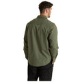 A person is standing with their back facing the viewer wearing an olive green button-up shirt and black pants in a neutral background.