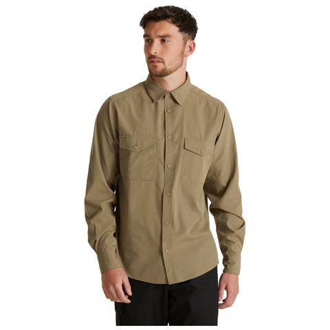 A man stands wearing a long-sleeve khaki shirt with buttoned front and two chest pockets, displaying a neutral expression in a plain light background.