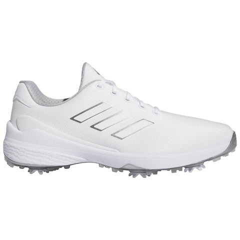A white athletic shoe features three silver stripes on the side with a textured upper and a rubber sole equipped with small spikes designed for traction on grass or turf surfaces.