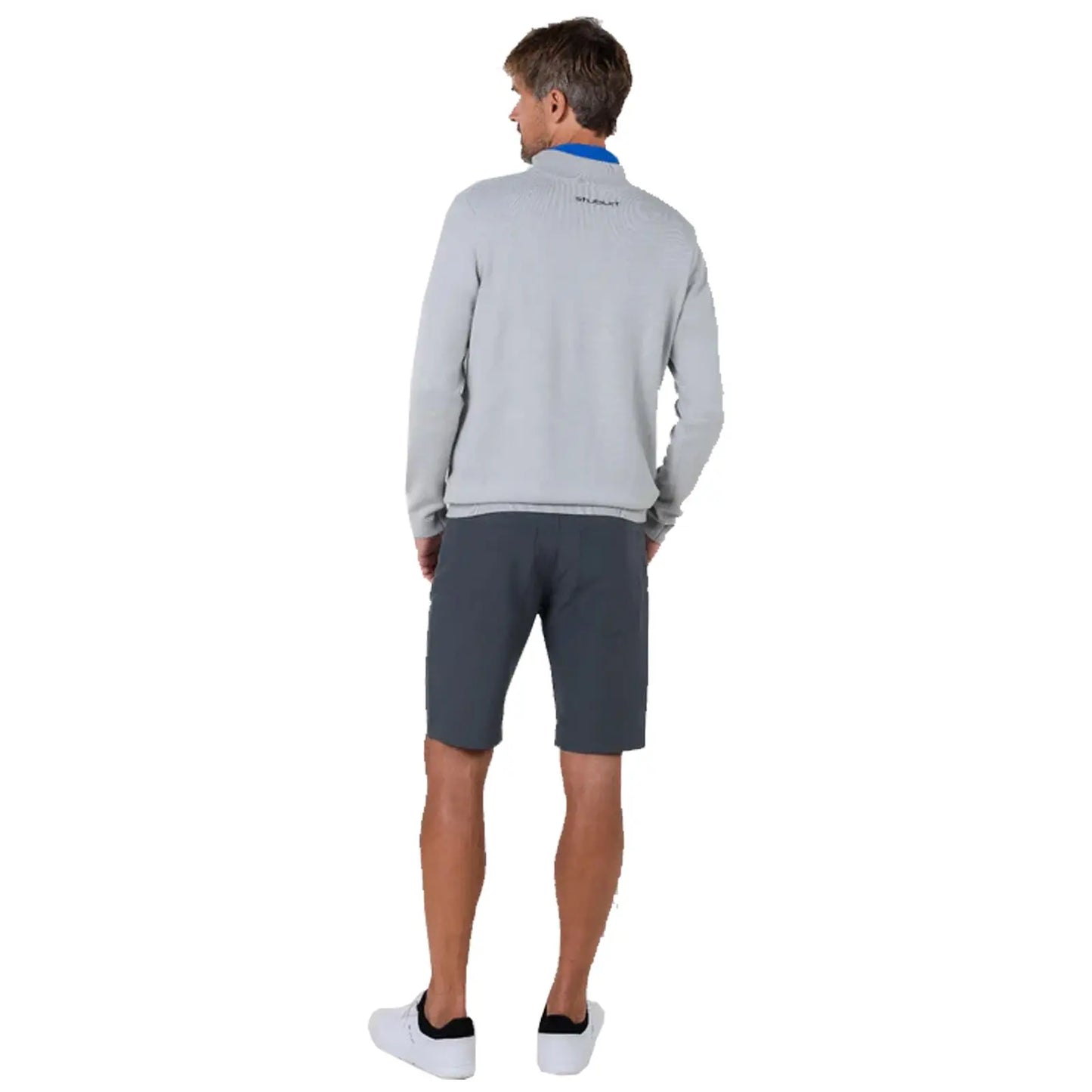 A man stands with his back turned wearing a grey sweater and dark shorts in a neutral backdrop, suggesting a casual, relaxed environment appropriate for outdoor activities.