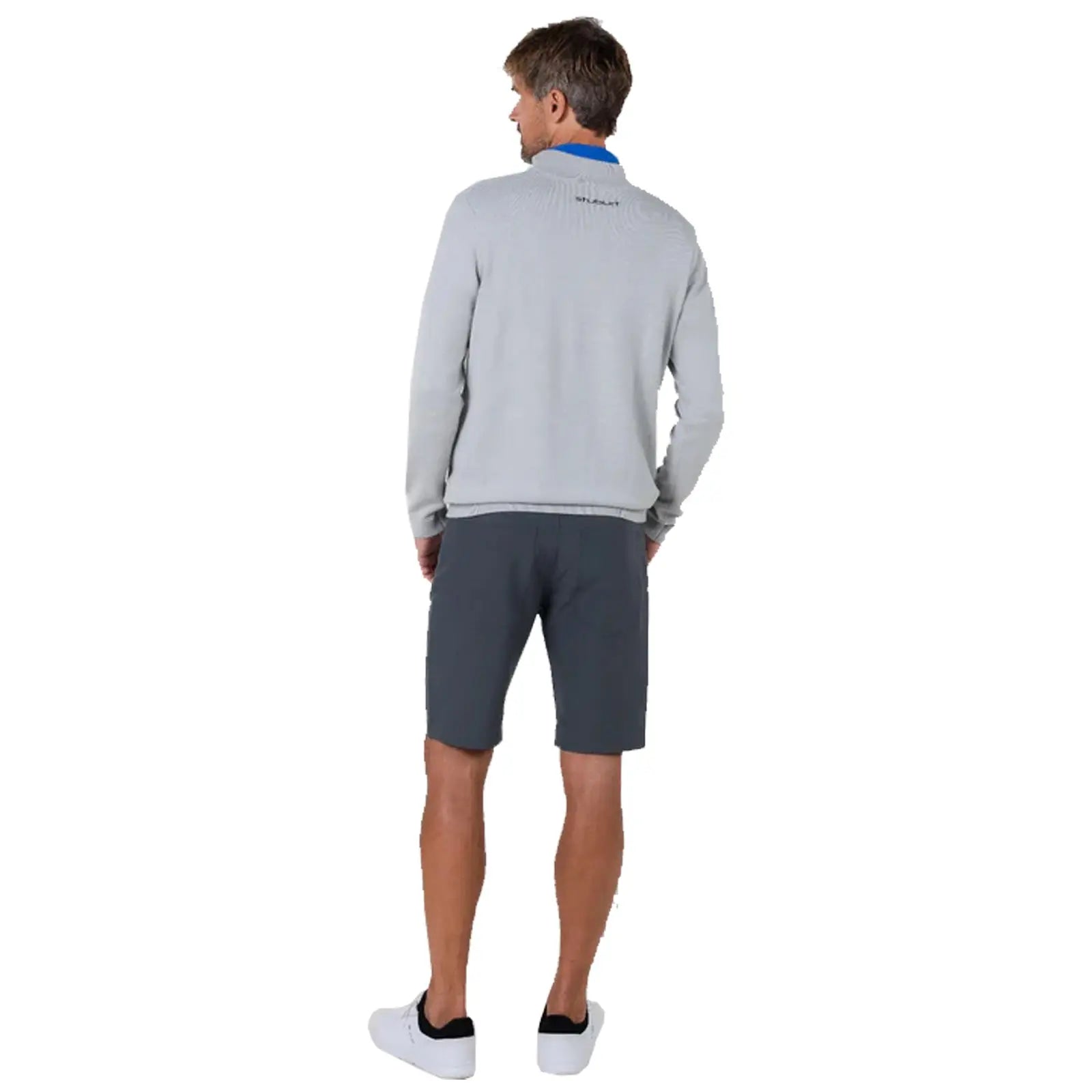 A man stands with his back turned wearing a grey sweater and dark shorts in a neutral backdrop, suggesting a casual, relaxed environment appropriate for outdoor activities.
