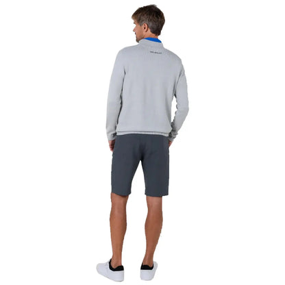 A man stands with his back turned wearing a grey sweater and dark shorts in a neutral backdrop, suggesting a casual, relaxed environment appropriate for outdoor activities.