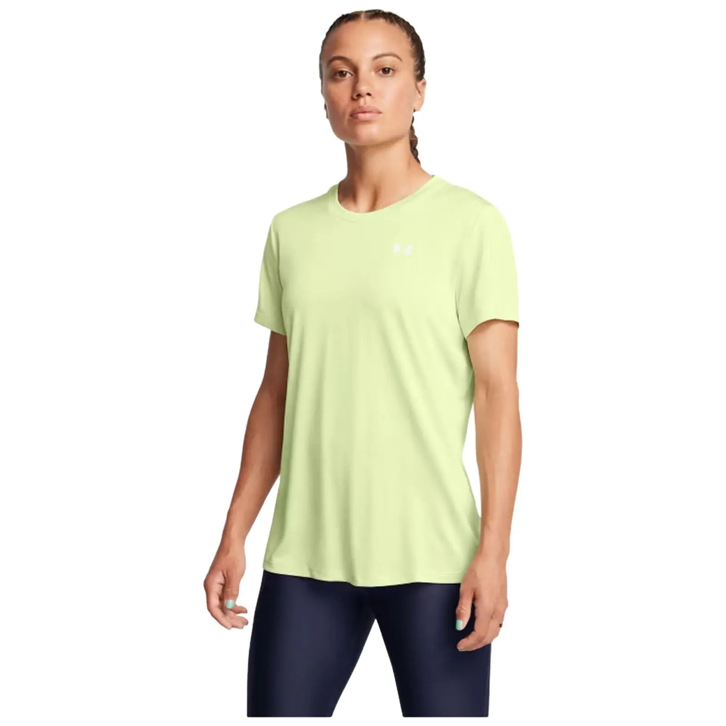 A woman stands confidently wearing a light green athletic shirt and dark leggings with her hair in a braid showcasing a neutral expression against a plain background.