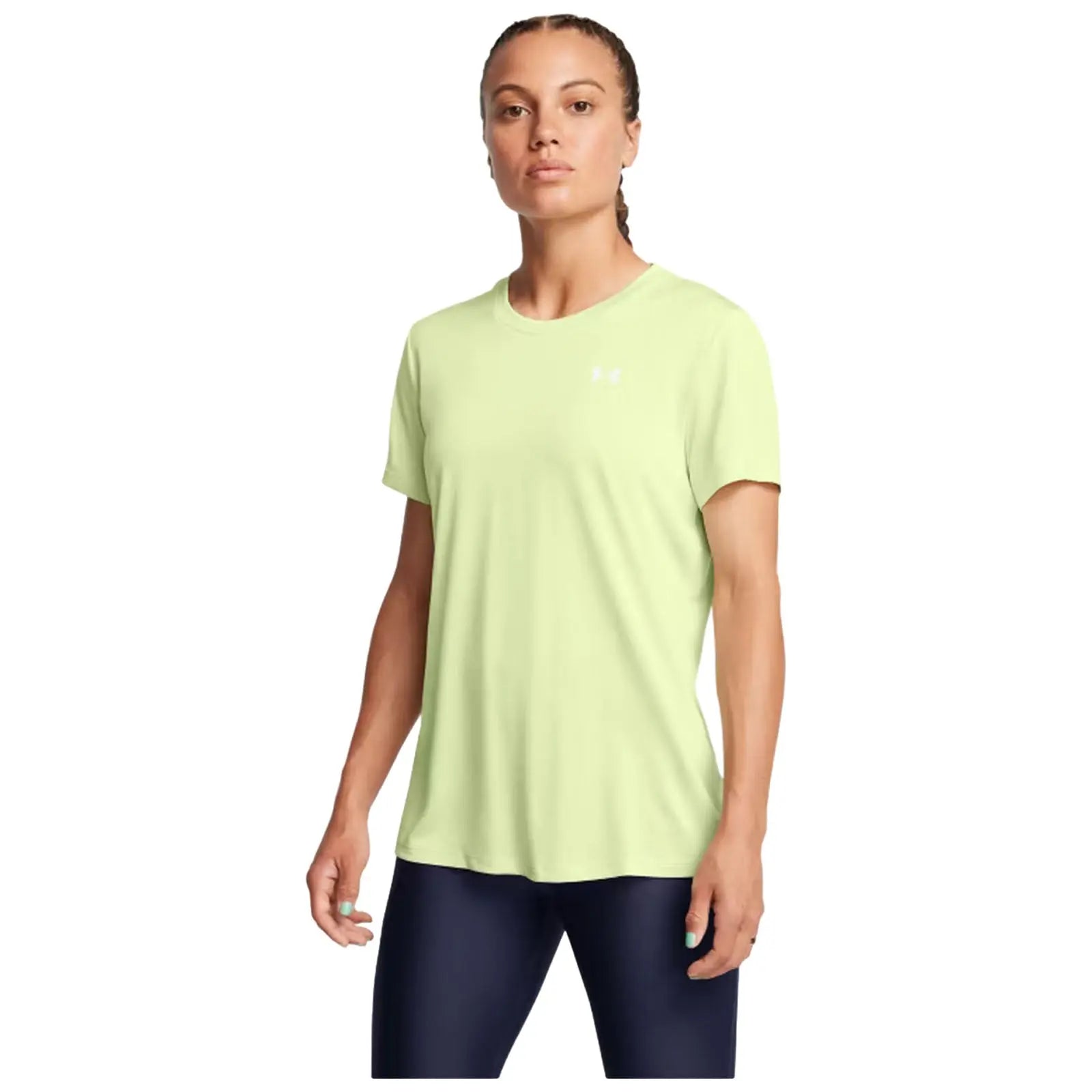 A woman stands confidently wearing a light green athletic shirt and dark leggings with her hair in a braid showcasing a neutral expression against a plain background.
