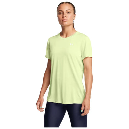 A woman stands confidently wearing a light green athletic shirt and dark leggings with her hair in a braid showcasing a neutral expression against a plain background.
