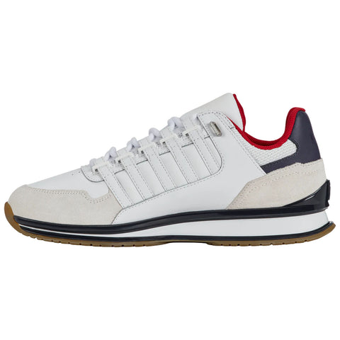 A white athletic shoe with red and navy accents sits on a light background showcasing its sleek design and textured materials intended for sports or casual wear.