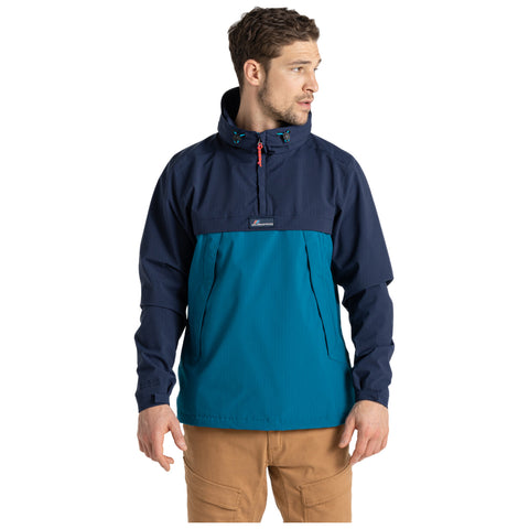 A man is wearing a colorful jacket with a navy upper section and a teal lower section while standing and looking to the side against a plain white background.
