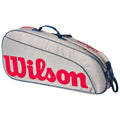 A gray tennis bag with red Wilson branding is positioned diagonally on a flat surface featuring a blue handle and a zipper along the top for easy access to contents.