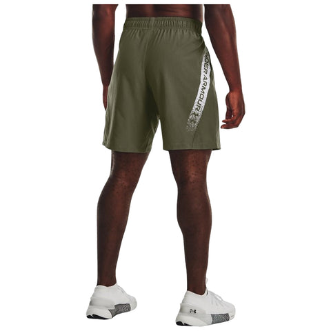 A person wearing khaki athletic shorts and white sneakers stands facing away the shorts feature a logo on the side in a sporty context.