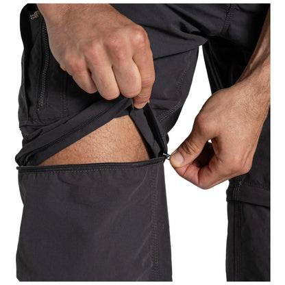 A person is unzipping the leg of a pair of dark trousers revealing bare skin underneath while adjusting the zipper with one hand in a neutral setting.