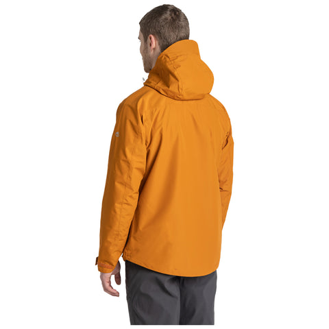 A person is standing facing away while wearing an orange jacket with a hood and grey pants in an undefined light background. The focus is on the jacket's color and design.