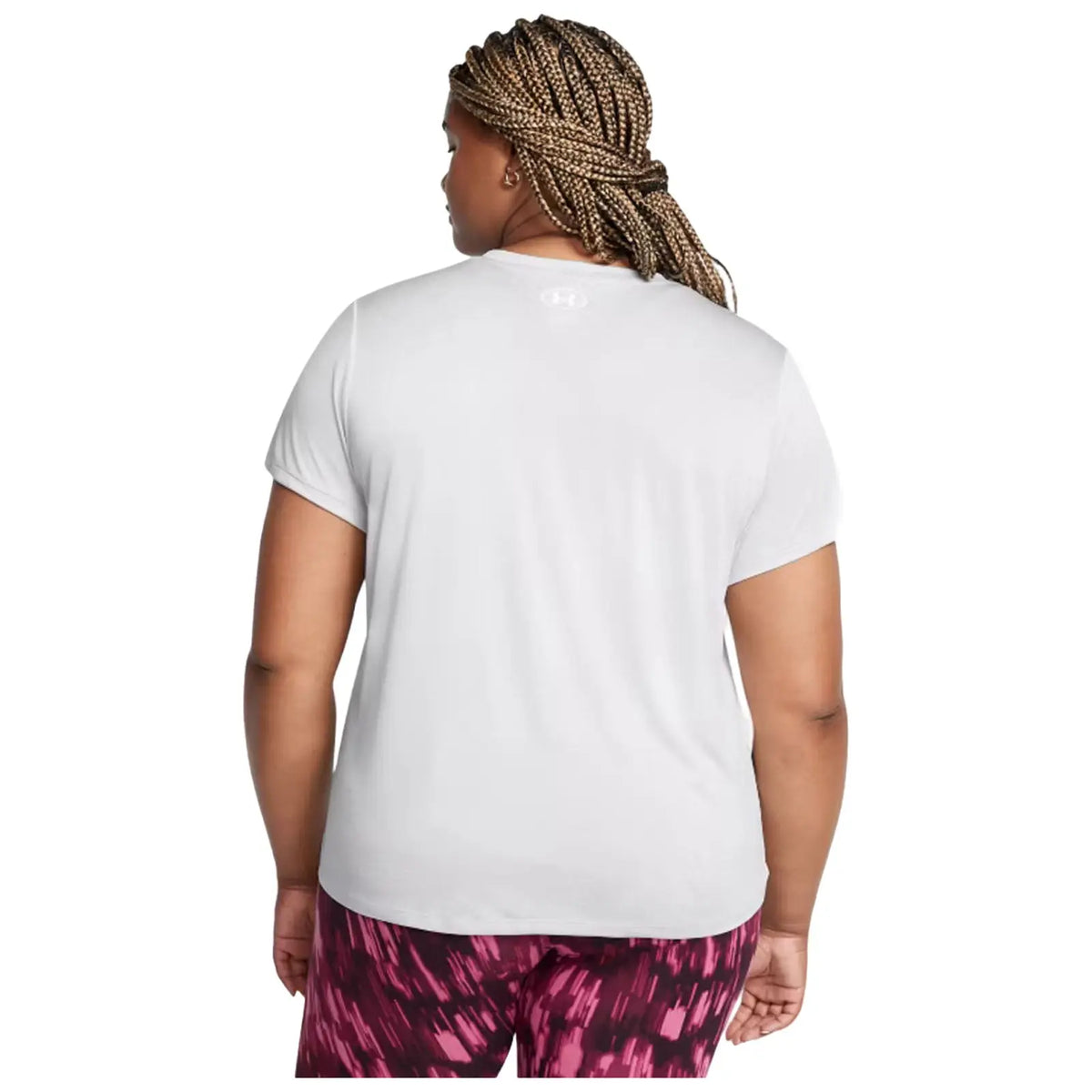 A person with braided hair is wearing a short-sleeved white shirt and patterned pink leggings while facing away in a neutral backdrop, suggesting a casual or athletic setting.