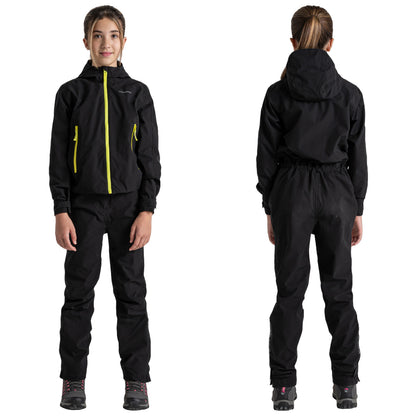 A child is wearing a black waterproof jacket and pants with bright yellow zippers and equipped with hiking boots standing in a neutral studio background.
