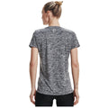 A woman stands facing away, wearing a short-sleeved, gray, textured athletic shirt. She has her hair tied up and her arms relaxed at her sides in a neutral background.