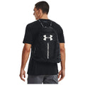 A man wearing a black t-shirt carries a black Under Armour backpack on his back while looking to the side in a neutral setting.